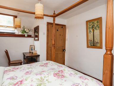 A bedroom with a wooden four poster bed a small wooden desk and chair a window with flowers on the sill and a framed picture on the wall at Llwyn Bedw in Nant Peris