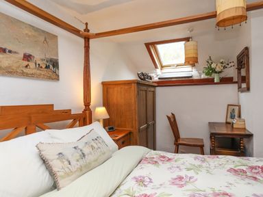 A bedroom with a wooden four-poster bed a bedside table with lamp a wooden wardrobe a chair and desk under a skylight window at Llwyn Bedw in Nant Peris