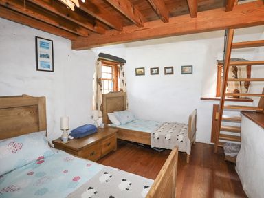 A bedroom with two wooden beds a wooden nightstand between them lamps and folded towels on the nightstand wooden ceiling beams and ladder leading up at Llwyn Bedw in Nant Peris