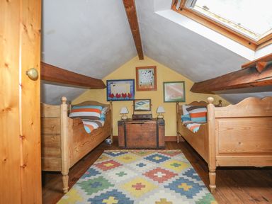 A bedroom with two wooden beds a colorful rug a chest with lamps and paintings on the wall at Llwyn Bedw in Nant Peris