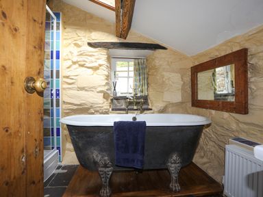 A bathroom with a clawfoot bathtub under a small window and a wooden framed mirror on the wall at Llwyn Bedw in Nant Peris