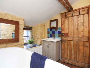 A bathroom with a white bathtub a wooden door a sink with a mirror and a small window with a plant on the windowsill at Llwyn Bedw in Nant Peris