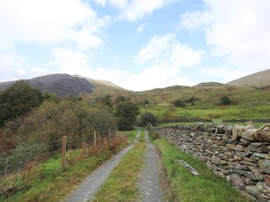 A gravel path through a grassy rural landscape with a stone wall on one side and wire fence on the other at Llwyn Bedw in Nant Peris