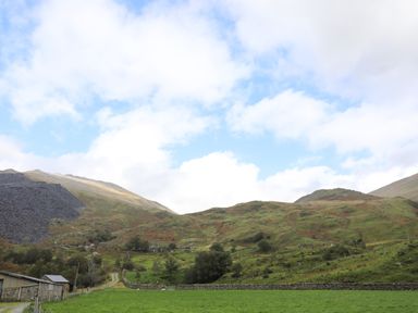 A rural landscape with green fields hills stone walls and a gravel path at Llwyn Bedw in Nant Peris