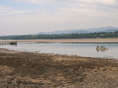 A view of a boat on the water near a pier with mountains in the background at Menai Cottage in Brynsiencyn