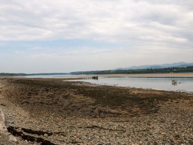 A view of the water and pier with rocks and a boat at Menai Cottage in Brynsiencyn
