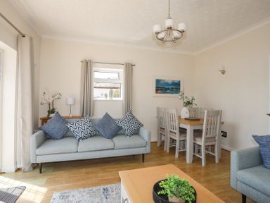 A living room with sofas pillows a dining table chairs and plants at Mermaid Cottage in Brynsiencyn