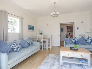 A living room with two sofas a coffee table a dining table with chairs and a chandelier at Mermaid Cottage Brynsiencyn