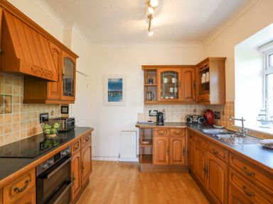 A kitchen with wooden cabinets black countertops and appliances at Mermaid Cottage in Brynsiencyn