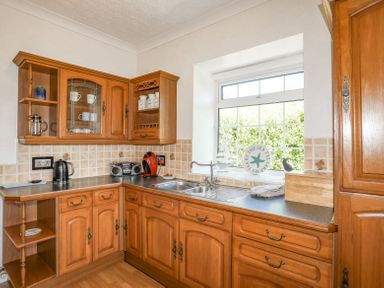 A kitchen with wooden cabinets a double sink a window and various kitchen appliances at Mermaid Cottage in Brynsiencyn