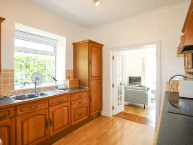 A kitchen with wooden cabinets and a double sink looking into a living room with a sofa and television at Mermaid Cottage in Brynsiencyn