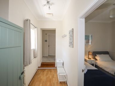 A hallway with wooden floor a window with curtains a coat rack and a door leading to a bedroom at Mermaid Cottage in Brynsiencyn