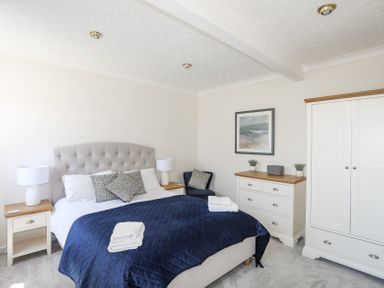 A bedroom with a bed covered by a blue quilt and white towels a wardrobe and a dresser at Mermaid Cottage in Brynsiencyn