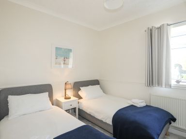 A bedroom with two single beds a nightstand with lamp a window with curtains and a picture on the wall at Mermaid Cottage in Brynsiencyn