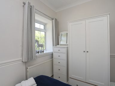 A bedroom corner with a window horse figurine on the sill white chest of drawers with mirror and wardrobe at Mermaid Cottage Brynsiencyn