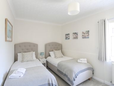 A bedroom with two single beds small bedside table lamp and window with curtains at Mermaid Cottage in Brynsiencyn