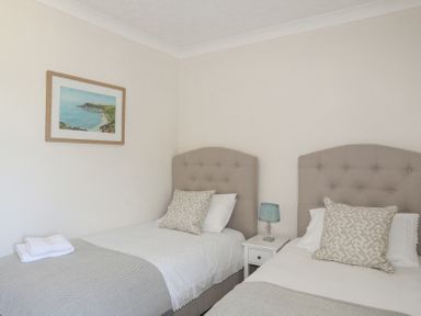 A bedroom with two single beds each with a patterned pillow a bedside table with a lamp and a framed coastal picture on the wall at Mermaid Cottage in Brynsiencyn