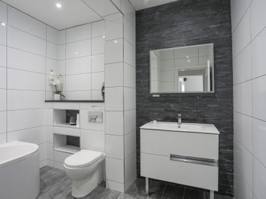 A bathroom with a toilet sink and mirror against tiled walls at Mermaid Cottage in Brynsiencyn