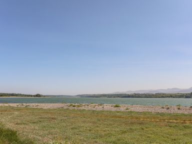 A grassy area with a gravel strip next to a body of water and hills in the background at Mermaid Cottage in Brynsiencyn