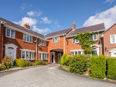 A row of brick townhouses with white-framed windows and doors surrounded by shrubs and bushes at Mews Cottage in Menai Bridge
