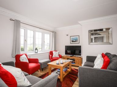 A living room with red and grey chairs a wooden coffee table a television and a mirror at Mews Cottage in Menai Bridge