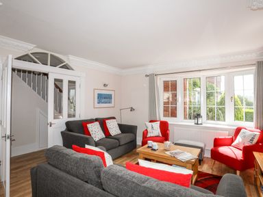 A sitting room with grey sofas, red armchairs, a wooden coffee table, and large windows at Mews Cottage in Menai Bridge