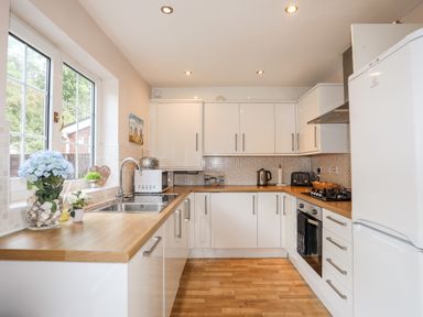A kitchen with white cabinets a wooden countertop a sink a refrigerator and a window showing outdoor trees at Mews Cottage Menai Bridge