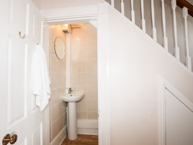 A small bathroom with a pedestal sink and round mirror under a staircase at Mews Cottage in Menai Bridge