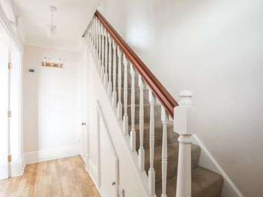A hallway with carpeted stairs and white wooden banister and wooden handrail at Mews Cottage in Menai Bridge
