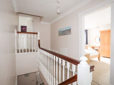 A hallway with a wooden and white banister leading to a bedroom with a wooden wardrobe and bed at Mews Cottage in Menai Bridge