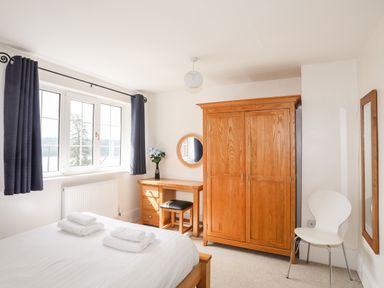 A bedroom with a bed towels on it a wooden wardrobe desk with a chair and a mirror at Mews Cottage in Menai Bridge