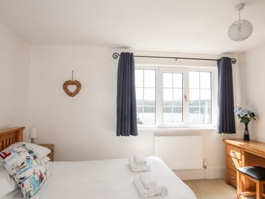 A bedroom with a bed with pillows and towels a window with curtains a wooden desk with a vase of flowers and a stool at Mews Cottage in Menai Bridge