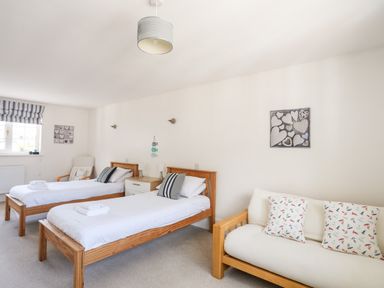 A bedroom with two single beds a white sofa with cushions and a chair at Mews Cottage in Menai Bridge