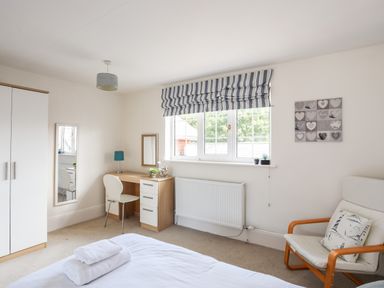 A bedroom with a bed with towels, a wardrobe, a desk with a chair and lamp, a window with striped blinds and an armchair at Mews Cottage in Menai Bridge