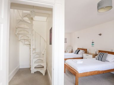 A white spiral staircase next to a bedroom with two wooden beds and striped pillows at Mews Cottage Menai Bridge
