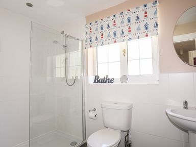 A bathroom with a shower enclosure toilet sink and round mirror at Mews Cottage in Menai Bridge