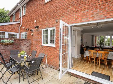 An outdoor patio with a table and chairs next to an open door leading into a dining area with a wooden table and chairs at Mews Cottage in Menai Bridge