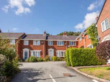 A row of red brick terraced houses with front doors and bushes along a curved street at Mews Cottage Menai Bridge