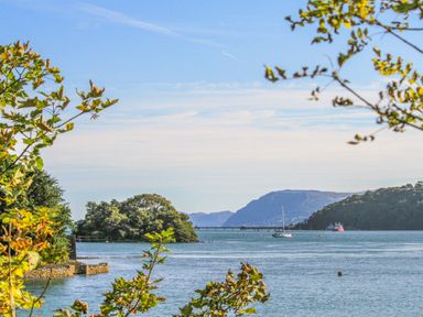 A coastal view with trees in the foreground boats on water and hills in the distance at Mews Cottage in Menai Bridge
