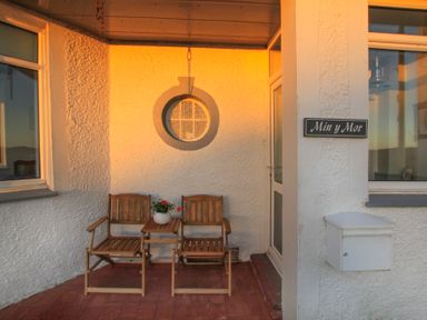 A small porch with two wooden chairs and a wooden table with a potted plant at Min Y Mor Trearddur Bay