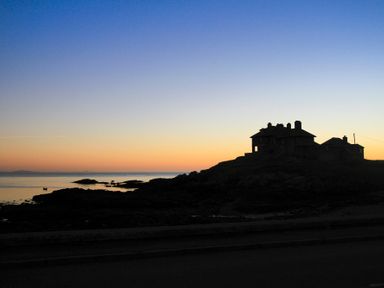 A silhouette of houses on a rocky shoreline with the sea and a sunset sky at Min Y Mor Trearddur Bay in Trearddur Bay