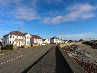 A road running alongside a row of houses and a beach with seaweed at Min Y Mor Trearddur Bay in Trearddur Bay