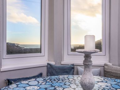 A table with a candle holder and cushions by two windows overlooking the sea at Min Y Mor Trearddur Bay in Trearddur Bay