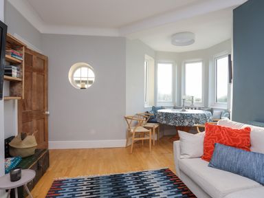 A living room with a sofa cushions a round dining table with chairs and windows at Min Y Mor Trearddur Bay