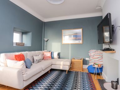A living room with a beige sectional sofa and colorful pillows a rug a wall-mounted TV and a framed picture at Min Y Mor Trearddur Bay in Trearddur Bay