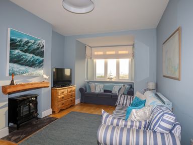 A living room with a striped sofa blue walls a wooden chest of drawers and a window with blinds at Min Y Mor Trearddur Bay