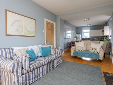 A living room with striped and beige sofas and a view into a kitchen at Min Y Mor Trearddur Bay