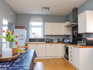 A kitchen with white cabinets wooden countertops a blue SMEG fridge and a table with tulips and fruit at Min Y Mor Trearddur Bay