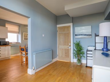 A room with blue walls wooden floor a wooden door a radiator a potted plant and a desk with a lamp at Min Y Mor Trearddur Bay