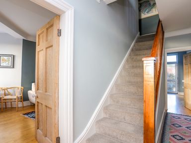 A stairway with carpet and wooden banister next to open wooden doors showing rooms with wooden chairs and a patterned rug at Min Y Mor Trearddur Bay